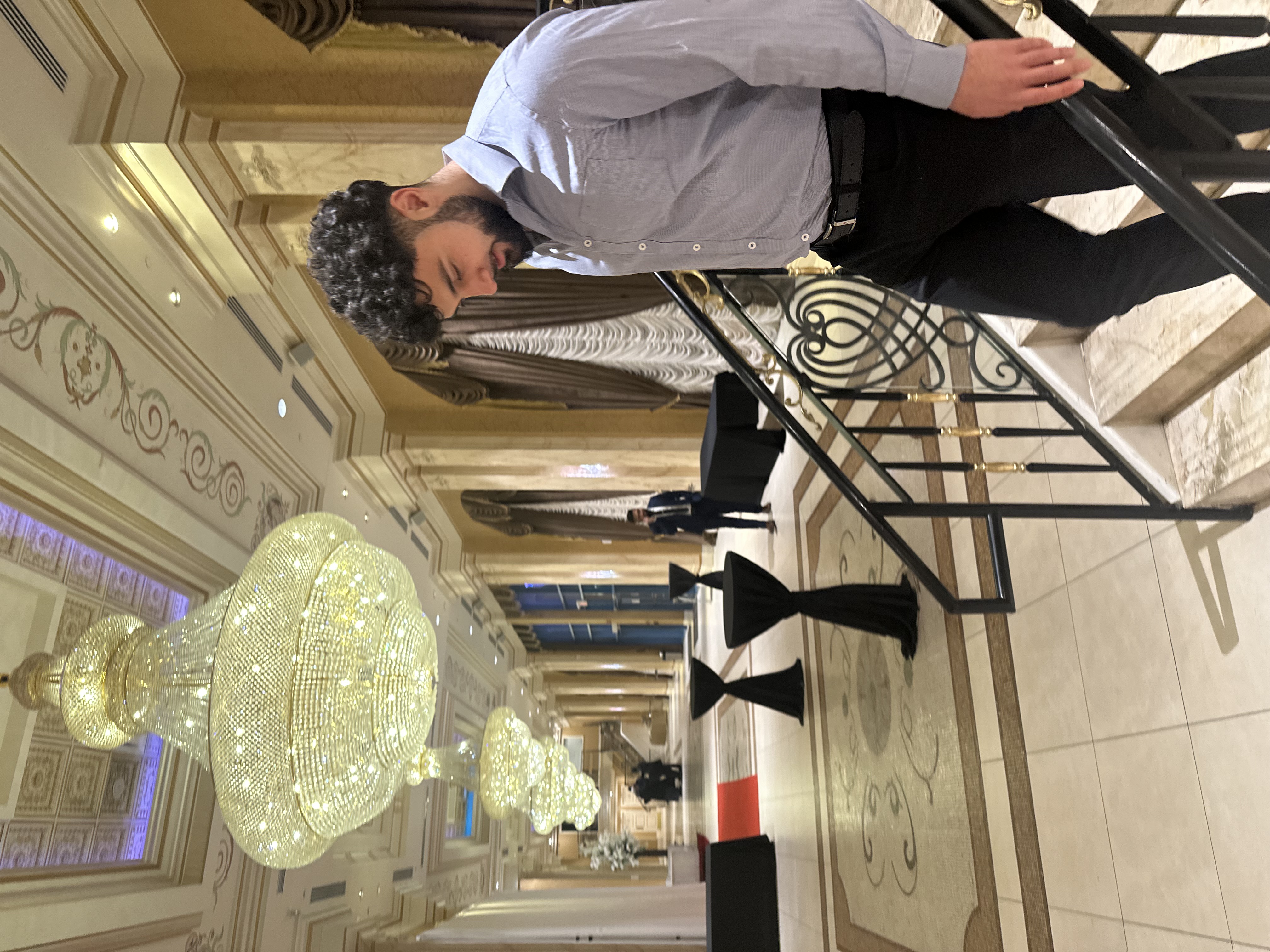 yousef walking down the stairs wearing a suit with chandeliers in the background.